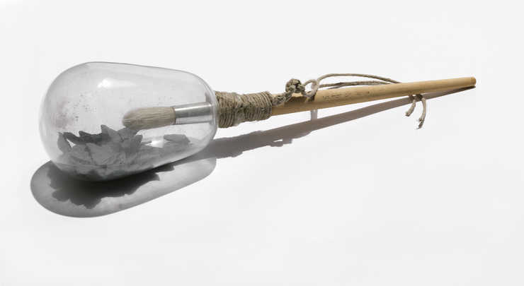 A rattle constructed of a paint brush with a large glass globe containing shards of shale...