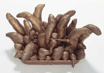 bronze colored potato-like forms protruding from a metal pan with a wire spatula resting on top