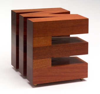 A wooden block carved into the form of the letter "M" on the top and the letter...