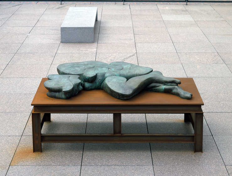 A flattened bronze woman lying on a steel table.