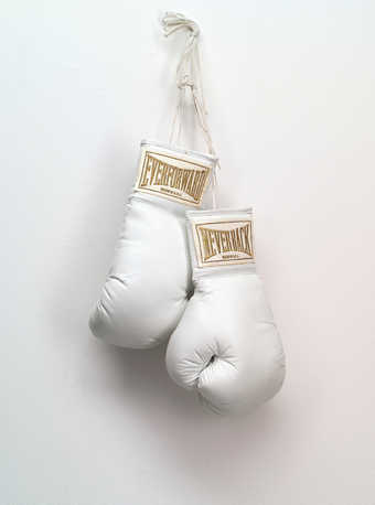 A pair of white boxing gloves with embroidered text on satin pieces on each cuff with the text...
