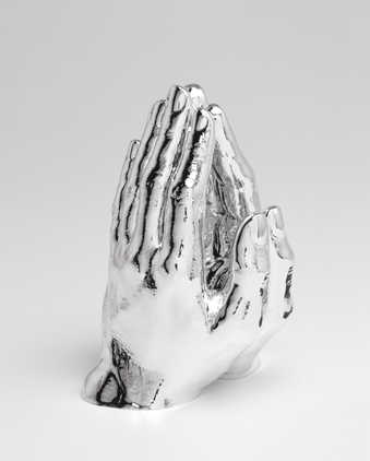 A pair of hands in a praying posture painted reflective silver.