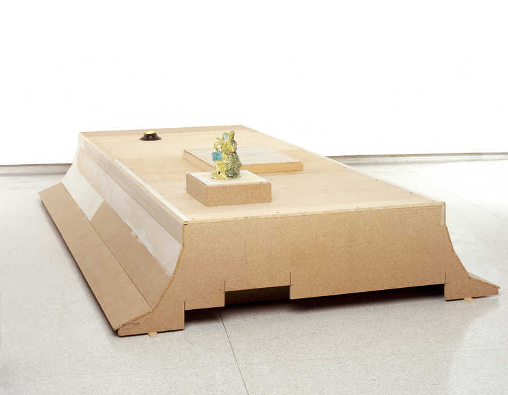 A large bench-like form with a light installed on one end and a ceramic vessel on the other