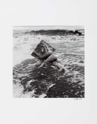 An image of a nude lying on a sandy beach with a mirror.  The model is Ana Mendieta