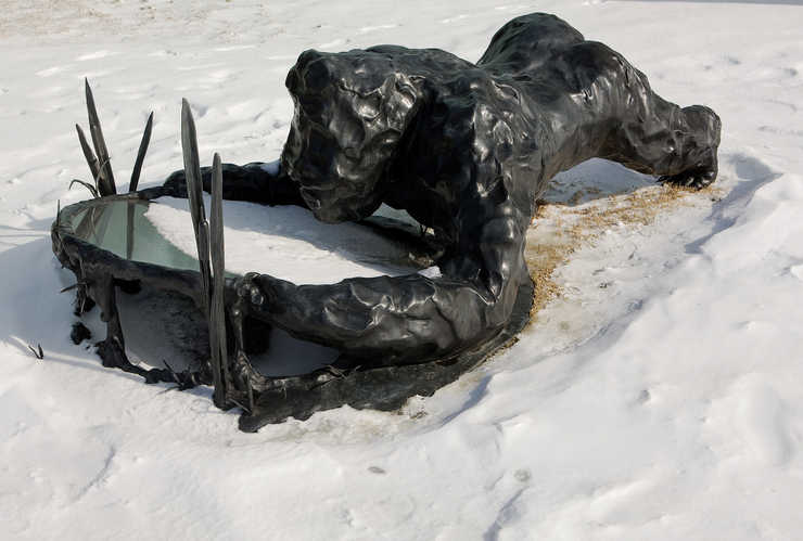 A bronze gorilla looking at its reflection in a piece of polished stainless-steel.