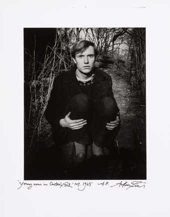 An image of a man crouching on a wooded path.