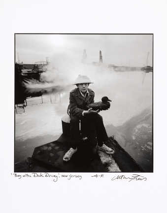 An image of a seated boy holding a duck decoy, in front of an industrial waterfall.