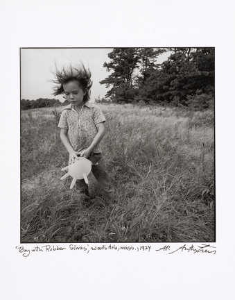 An image of a boy holding an inflated rubber glove at his waist, while walking in a field